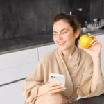 close-up-portrait-happy-young-woman-bathrobe-sitting-kitchen-using-mobile-phone_1258-195021